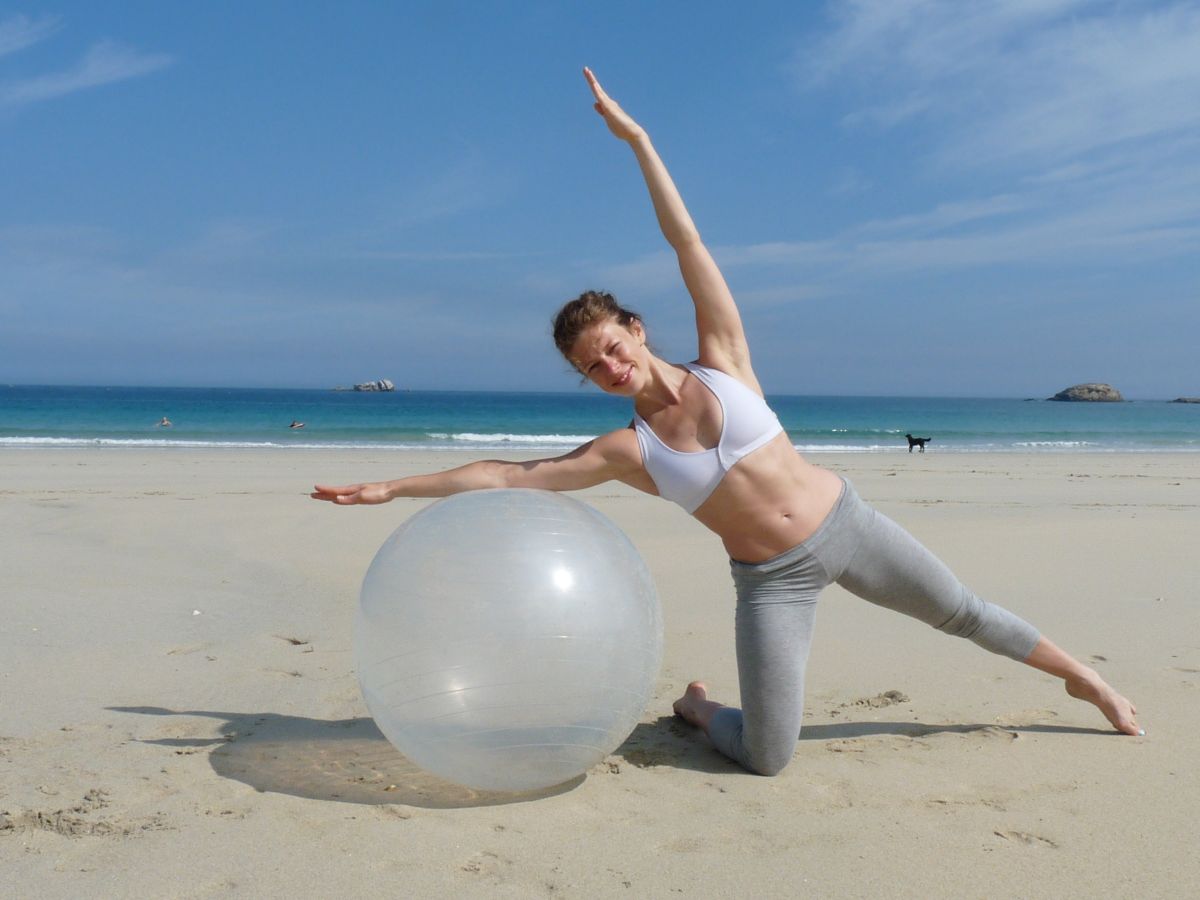 Gabrielle Eychenne pratiquant un exercice de Pilates avec ballon sur une plage en Bretagne